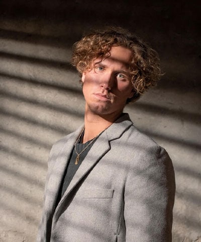 A man with curly hair standing in front of a wall.